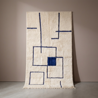 Tapis Berbère Mrirt écru à motifs géométriques bleus, vue de face sur fond gris studio