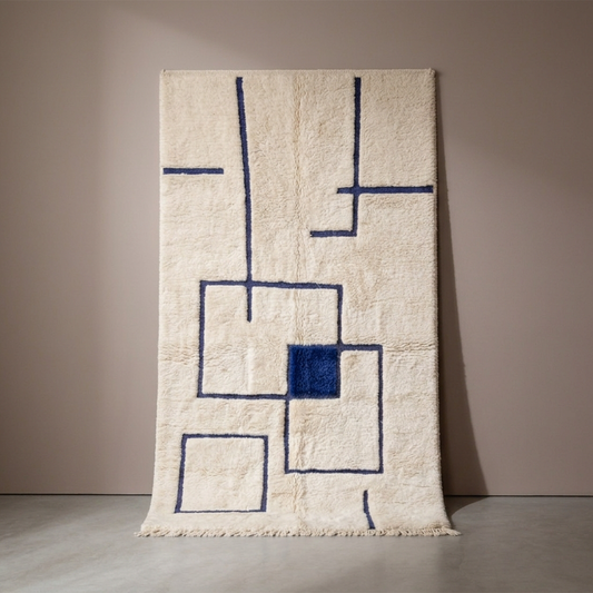 Tapis Berbère Mrirt écru à motifs géométriques bleus, vue de face sur fond gris studio